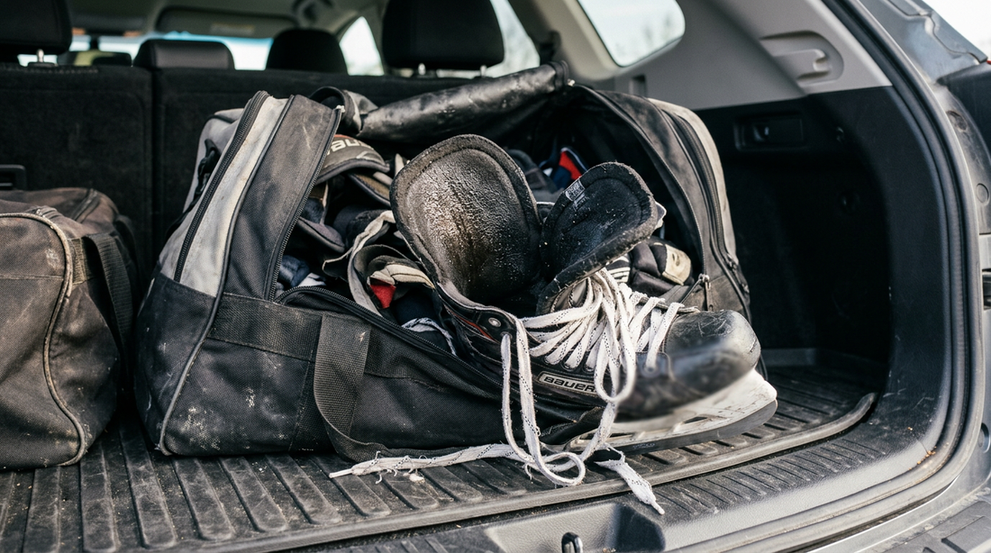 A hockey bag in a car trunk with damp skates and frayed laces after a tournament weekend.