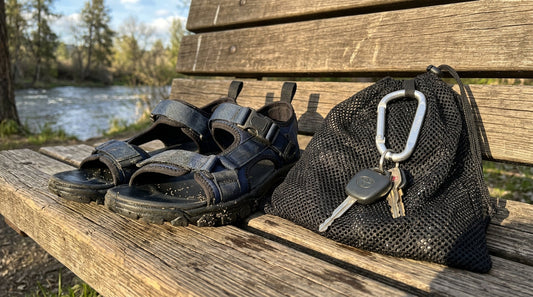 A flatlay of neoprene river sandals, a mesh gear bag, and car keys on a wooden surface to prevent smelly river shoes in a car.
