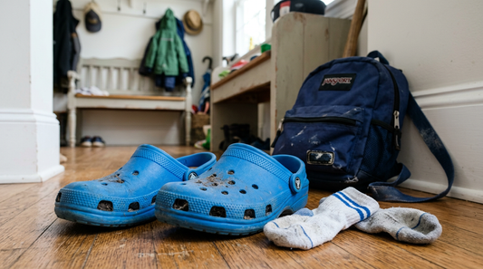 A pair of bright blue kids foam clogs kicked off next to dirty socks and a child's school backpack in a mudroom entryway.