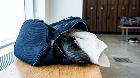 An open professional gym bag on a wooden locker room bench with soccer cleats and an athletic towel.