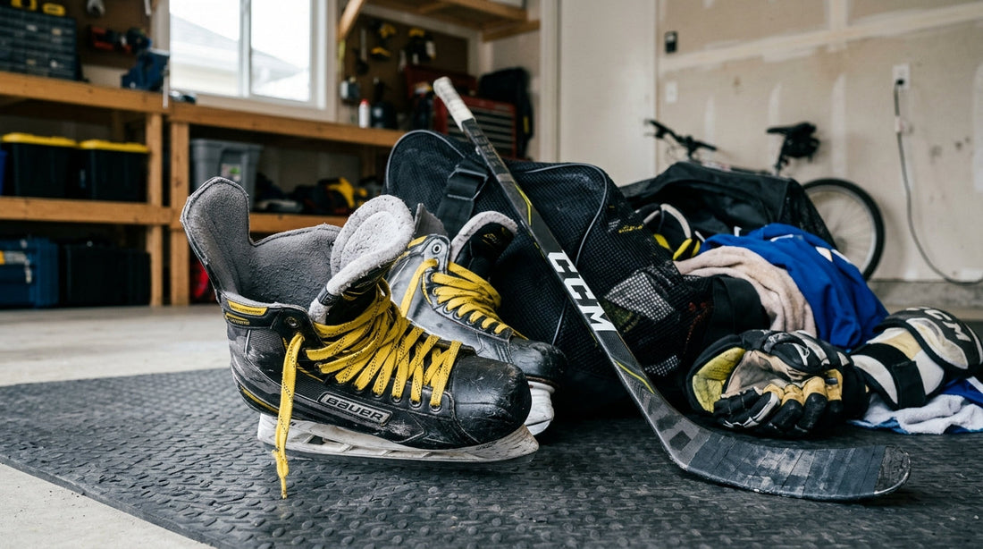 A pair of professional ice hockey skates with yellow laces and a black composite hockey stick leaning against an unzipped mesh gear bag in a garage.