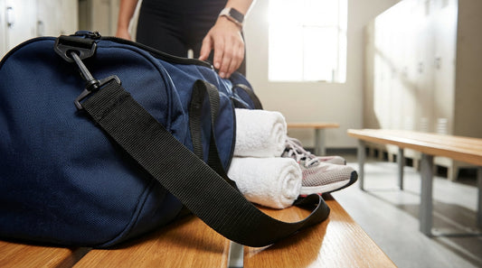 An open nylon gym bag with rolled towels and athletic gear on a wooden locker room bench