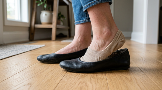 Black leather ballet flats on a hardwood floor with a bunched-up no-show sock showing why flats smell without socks.